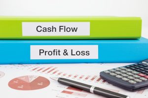 Cash Flow, Profit & Loss words on labels with document binders, graphs and business reports